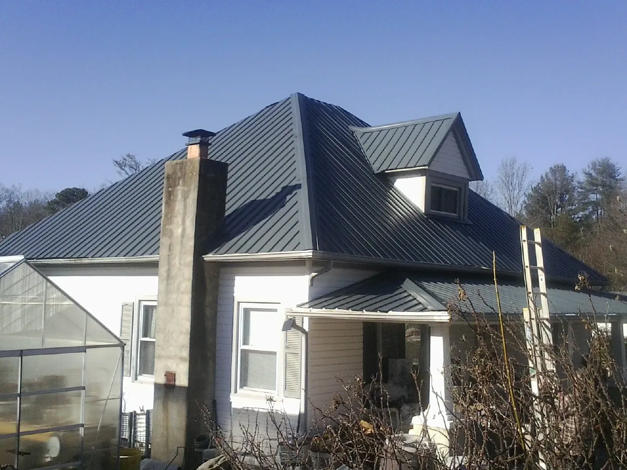 Dark blue standing seam metal roof on a white farmhouse with dormer — Slate & Tile Roof Repair by Roofing Brothers in Martville