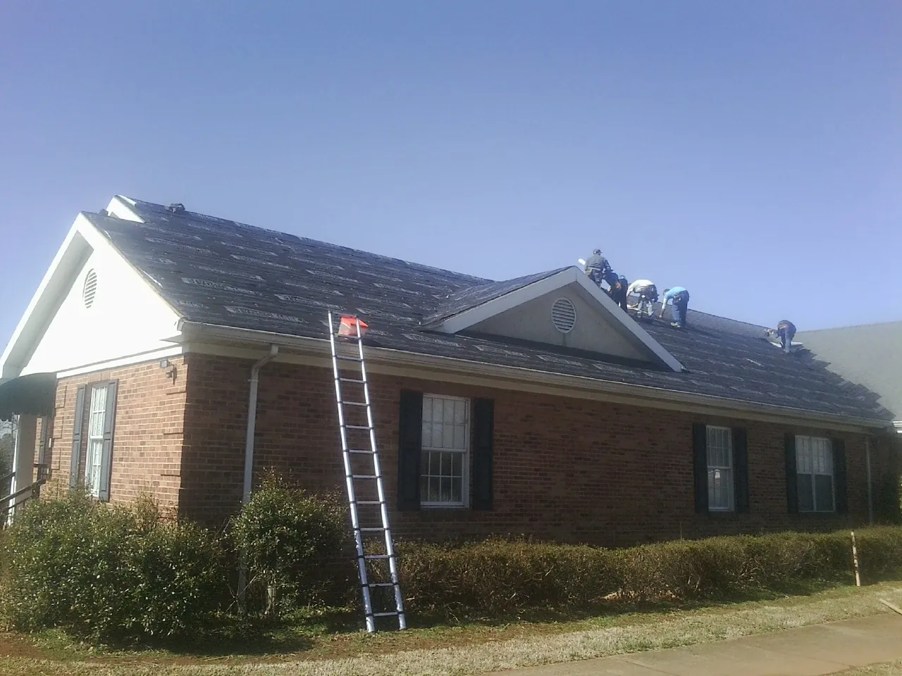 Crew tearing shingles off a brick ranch roof with a ladder set — Emergency Roof Repair work by our crew in Martville
