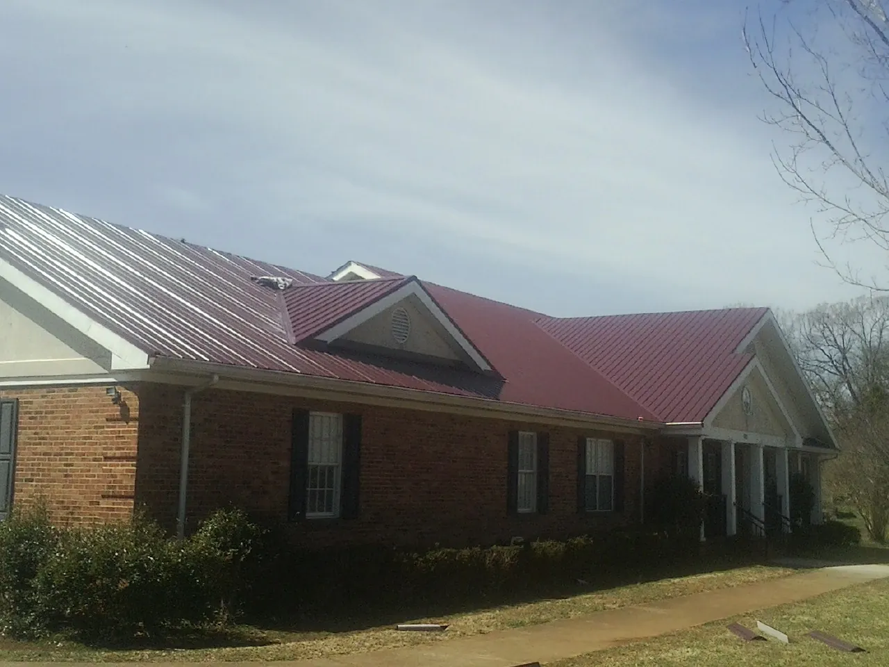 Red metal roof with gabled entries on a long brick building, from a Hail Damage Roof Repair job in Martville