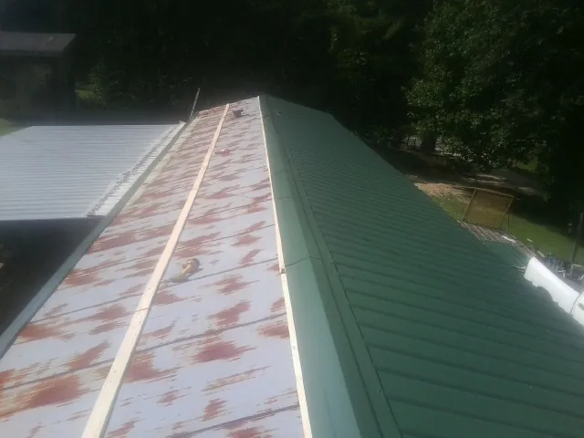 Old rusted panels beside newly installed green metal roofing — Wind Damage Roof Repair by Roofing Brothers in Martville