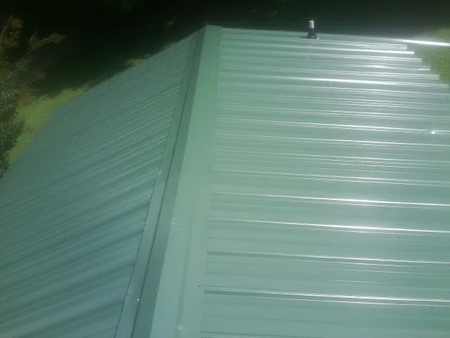 New green metal panels meeting at the ridge of a roof — Flat Roof Repair work by our crew in Martville