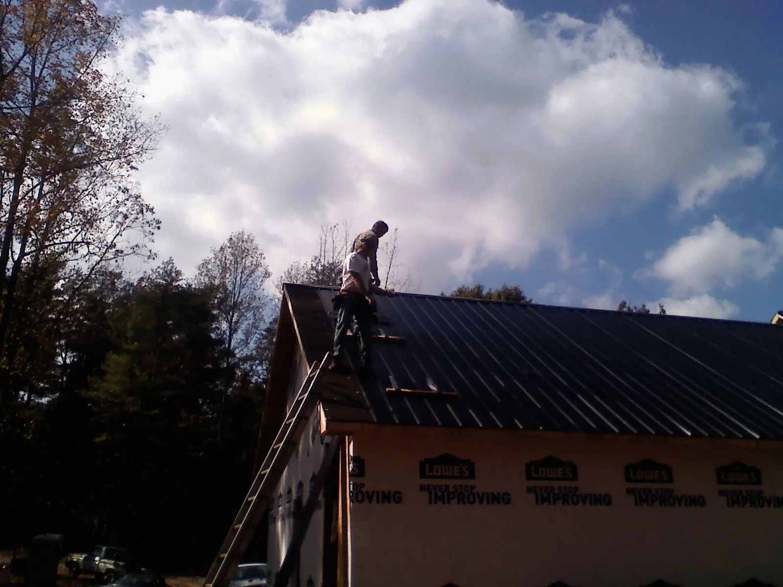 Roofer fastening dark metal panels high against a cloudy sky, from a Roof Inspection job in Martville