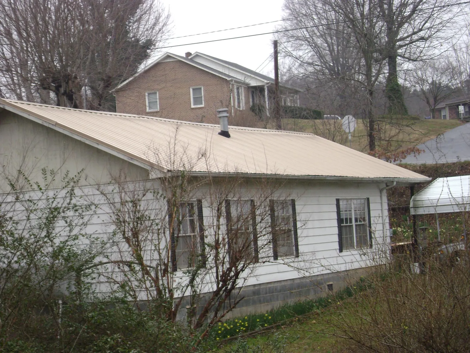 Tan metal roof on a white sided house set into a hillside — Commercial Roofing by Roofing Brothers in Martville