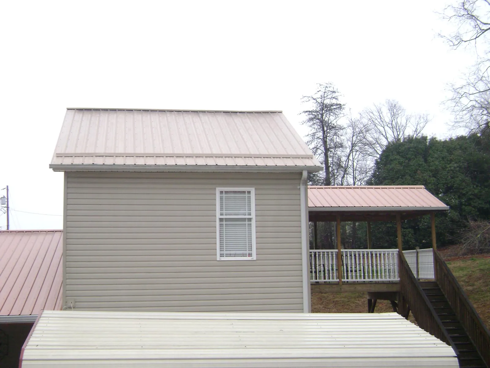 Tan metal roofs on a two story addition and attached porch, from a Roof Replacement job in Martville